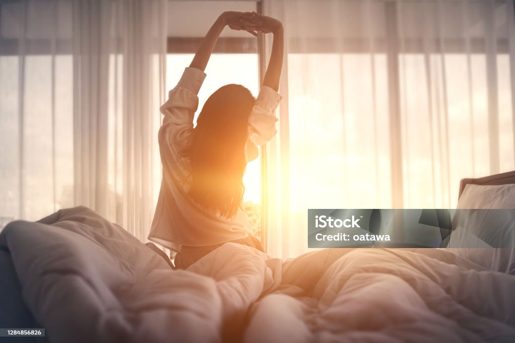 Kvinna som stretchar i morgonsol vid fönster – lugn och nystart
